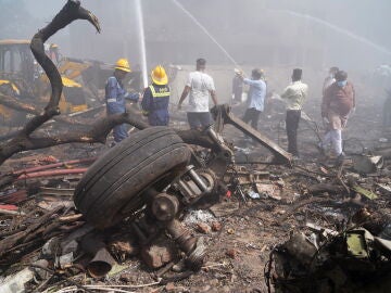 Unas personas apagan el fuego junto a los escombros en el lugar donde se estrelló este jueves un avión de Air India