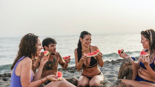 Grupo de amigos comiendo fruta en la playa