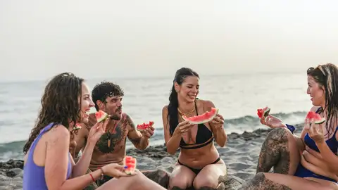 Grupo de amigos comiendo fruta en la playa Grupo de amigos comiendo fruta en la playa