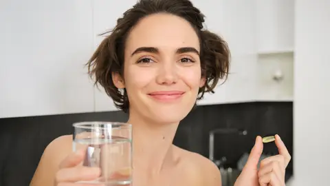 Mujer con un vaso de agua y una cápsula en la mano Mujer con un vaso de agua y una cápsula en la mano