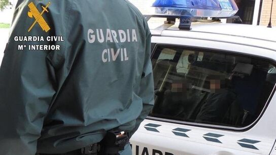 Agente de la Guardia Civil junto a un coche patrulla. 