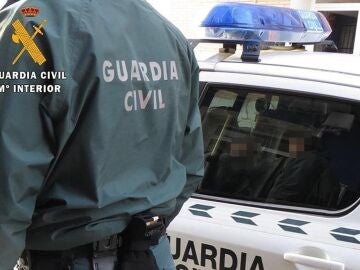 Agente de la Guardia Civil junto a un coche patrulla. 