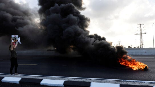 Un manifestante sostiene una foto de un reh&eacute;n israel&iacute; mientras los manifestantes bloquean una carretera
