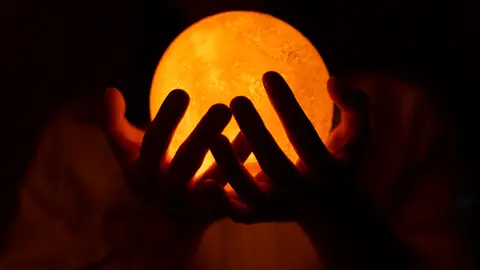 Unas manos sostienen una luz que parece la Luna Unas manos sostienen una luz que parece la Luna