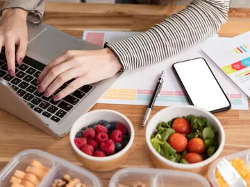 Una mujer con el ordenador rodeada de comida Una mujer con el ordenador rodeada de comida