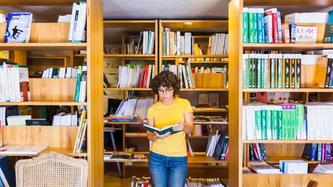 Una mujer leyendo rodeada de estanterías con libros Una mujer leyendo rodeada de estanterías con libros