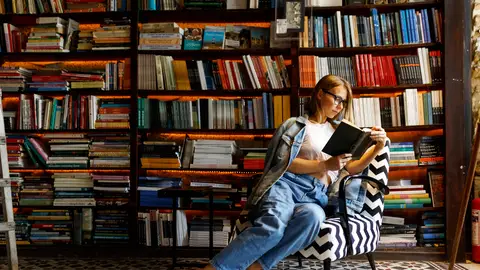 Mujer leyendo rodeada de estanterías de libros Mujer leyendo rodeada de estanterías de libros