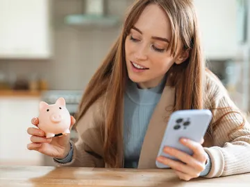 Una mujer joven con una hucha y un móvil Una mujer joven con una hucha y un móvil