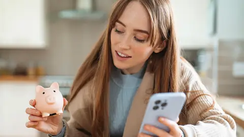 Una mujer joven con una hucha y un móvil Una mujer joven con una hucha y un móvil