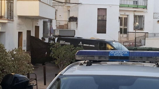  Coches de la Guardia Civil y de los servicios funerarios junto a la vivienda (izquierda) en Torrox (M&aacute;laga), donde este martes han fallecido cuatro personas de una misma familia por inhalaci&oacute;n de gas 