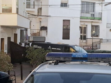  Coches de la Guardia Civil y de los servicios funerarios junto a la vivienda (izquierda) en Torrox (M&aacute;laga), donde este martes han fallecido cuatro personas de una misma familia por inhalaci&oacute;n de gas 