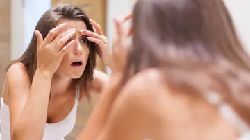Una mujer con cara de susto miranso su piel frente al espejo. Una mujer con cara de susto miranso su piel frente al espejo.