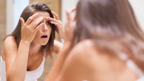 Una mujer con cara de susto miranso su piel frente al espejo. Una mujer con cara de susto miranso su piel frente al espejo.