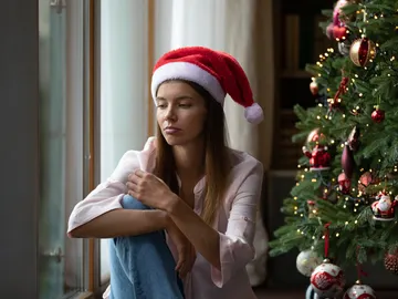 Una mujer pensativa junto al árbol de Navidad Una mujer pensativa junto al árbol de Navidad