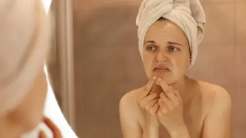 Una mujer con cara de disgusto frente al espejo Una mujer con cara de disgusto frente al espejo