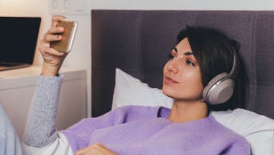 Mujer en la cama mirando una pel&iacute;cula con el tel&eacute;fono