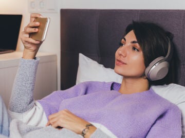 Mujer en la cama mirando una pel&iacute;cula con el tel&eacute;fono