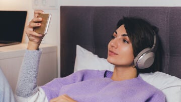 Mujer en la cama mirando una pel&iacute;cula con el tel&eacute;fono