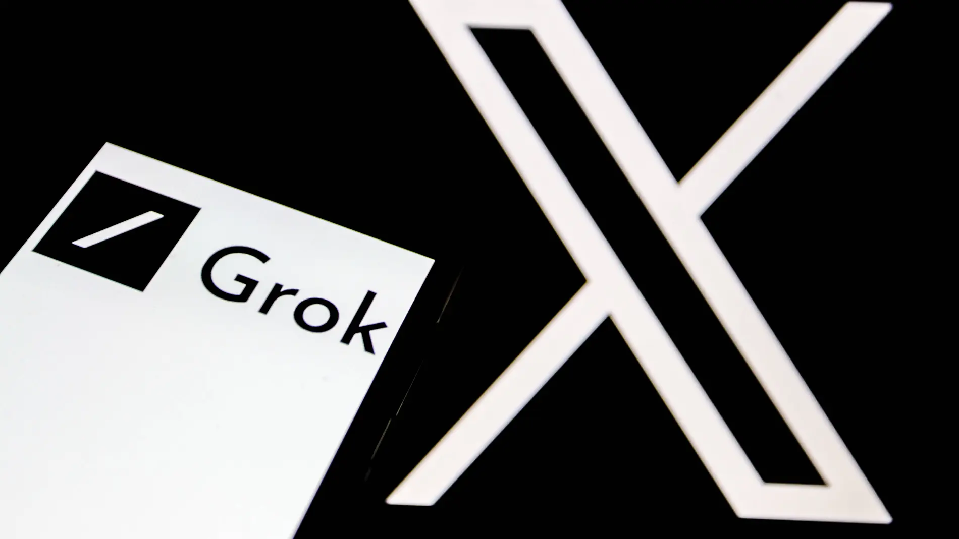 El logo de Grok aparece en la pantalla de un smartphone, y al fondo, el logo de la red social 'X' El logo de Grok aparece en la pantalla de un smartphone, y al fondo, el logo de la red social 'X'