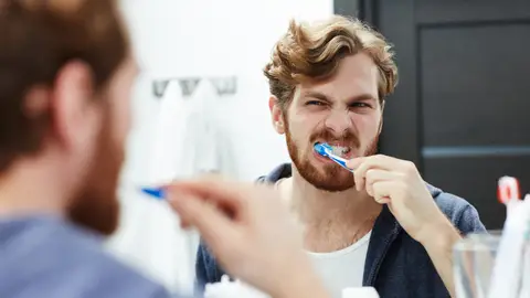 Hombre cepillándose los dientes con cara de dolor Hombre cepillándose los dientes con cara de dolor