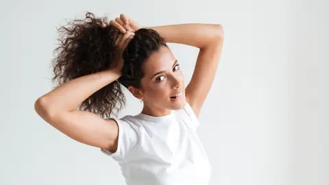 Mujer de pelo rizado recogiéndoselo en una coleta Mujer de pelo rizado recogiéndoselo en una coleta