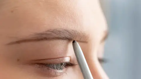 Mujer rellenando su ceja recta con un lápiz fino Mujer rellenando su ceja recta con un lápiz fino