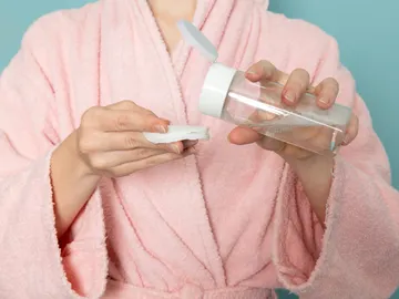 Mujer con un bote de agua micelar y un disco de algodón en la mano Mujer con un bote de agua micelar y un disco de algodón en la mano