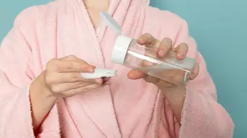 Mujer con un bote de agua micelar y un disco de algodón en la mano Mujer con un bote de agua micelar y un disco de algodón en la mano