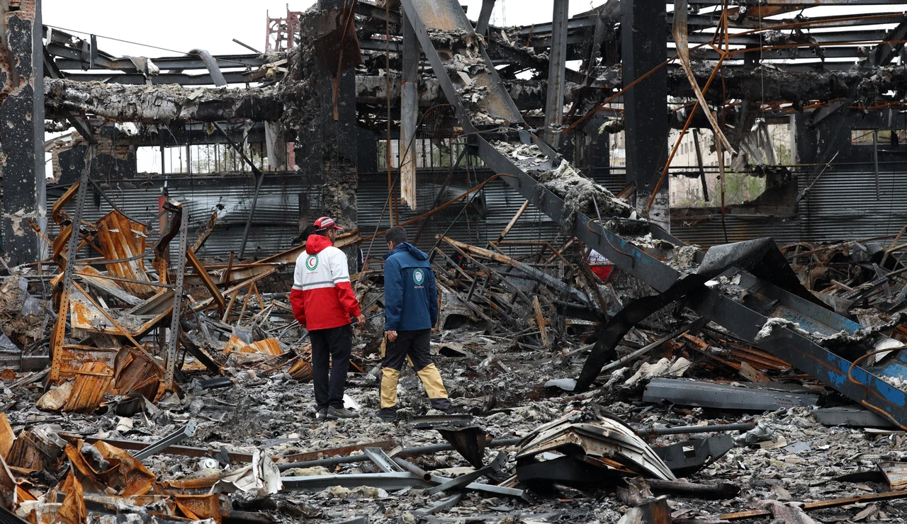 Miembros de la Media Luna Roja Iraní se encuentran entre los restos de vehículos en un taller mecánico en Teherán