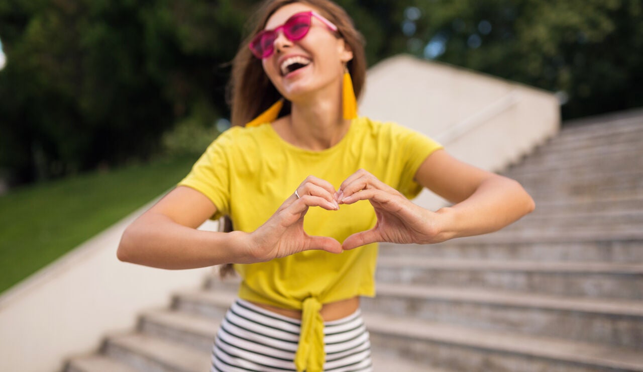 Mujer feliz con una camiseta amarilla haciendo el s&iacute;mbolo de coraz&oacute;n con las manos