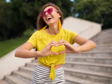 Mujer feliz con una camiseta amarilla haciendo el símbolo de corazón con las manos Mujer feliz con una camiseta amarilla haciendo el símbolo de corazón con las manos