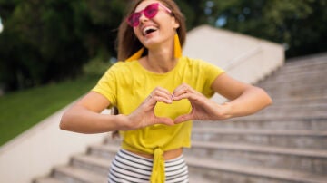 Mujer feliz con una camiseta amarilla haciendo el s&iacute;mbolo de coraz&oacute;n con las manos