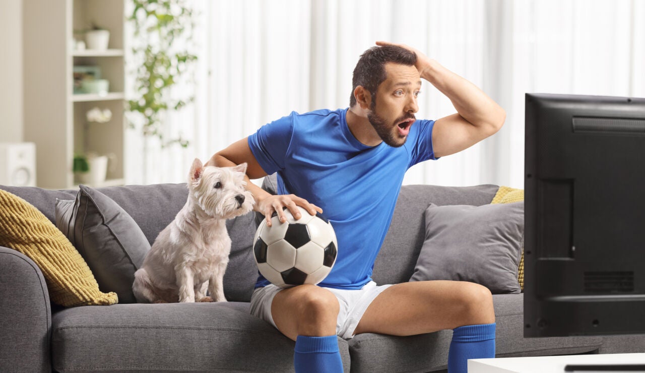 Un hombre viendo el f&uacute;tbol con su perro al lado
