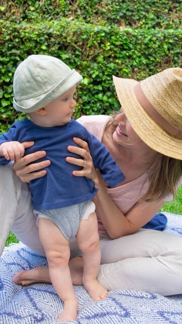 Un bebé con gorro y camiseta en verano junto a su madre