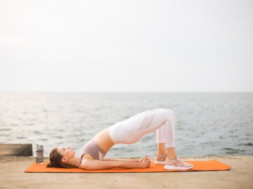 Mujer practicando puente de gl&uacute;teos en la playa