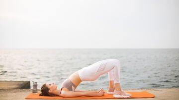 Mujer practicando puente de gl&uacute;teos en la playa