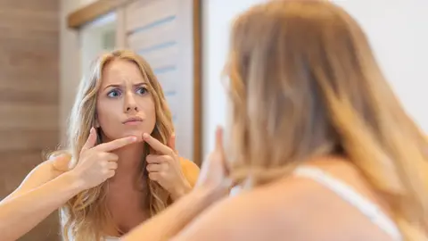 Mujer tocándose un grano Mujer tocándose un grano