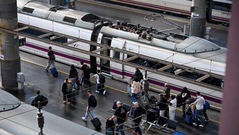 Varios pasajeros pasan ante un AVE en la Estaci&oacute;n de Atocha