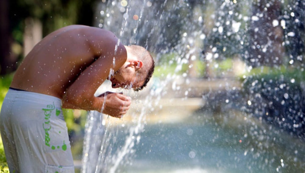 Un joven refrescándose en una fuente