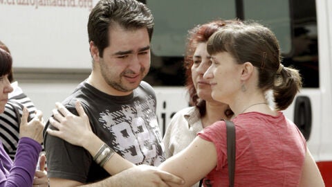 Un grupo de personas consuela al compa&ntilde;ero de la lotera asesinada en M&oacute;stoles