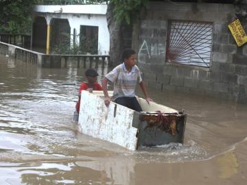 Un joven trabaja transportando a otro en medio de una calle inundada
