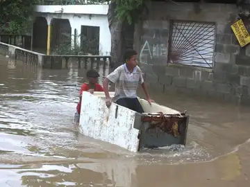 Un joven trabaja transportando a otro en medio de una calle inundada Un joven trabaja transportando a otro en medio de una calle inundada