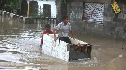Un joven trabaja transportando a otro en medio de una calle inundada Un joven trabaja transportando a otro en medio de una calle inundada