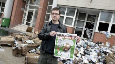 El editor del semanario frente a la sede de la revista y con portada de la pol&eacute;mica