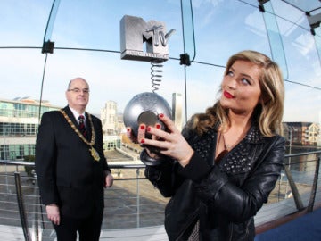 El alcalde de Belfast, Pat Convery, (al fondo), posa junto a la estatuilla, en manos de una reportera de la cadena. 