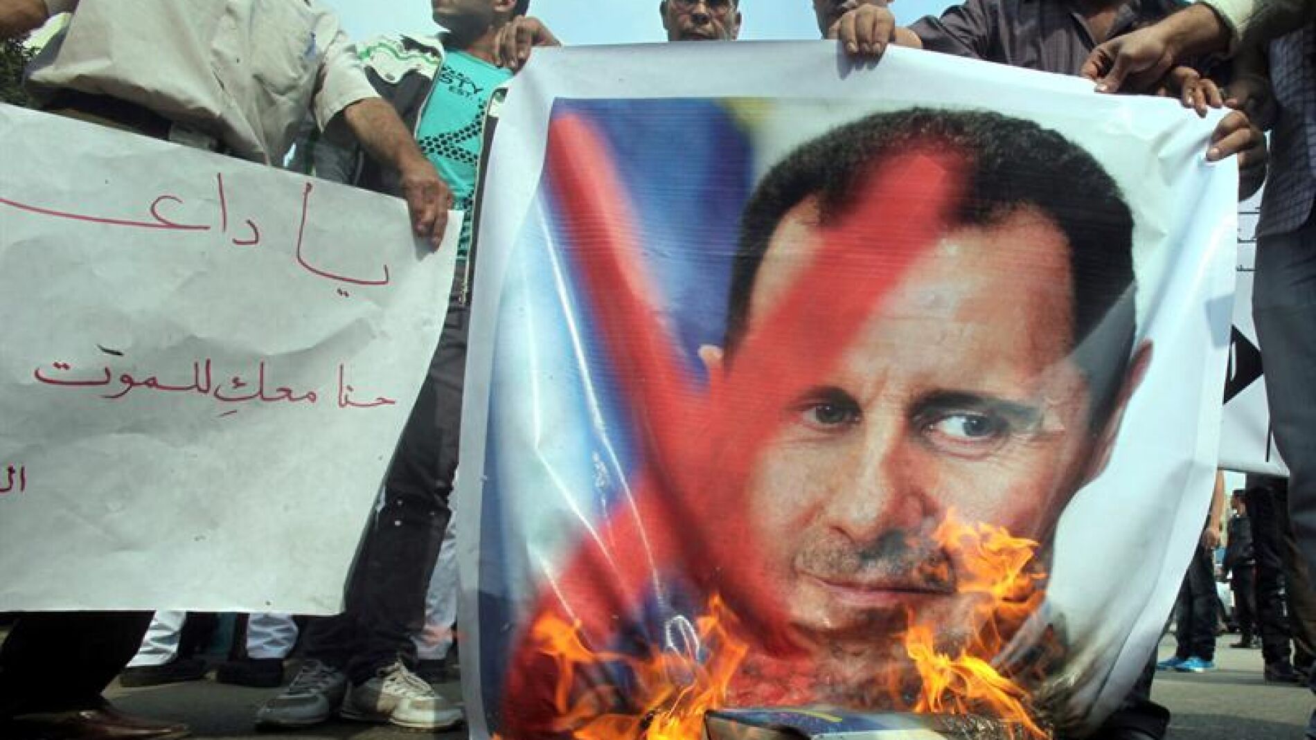 Manifestantes queman una pancarta con la fotograf&iacute;a del presidente sirio, Bachar al Asad