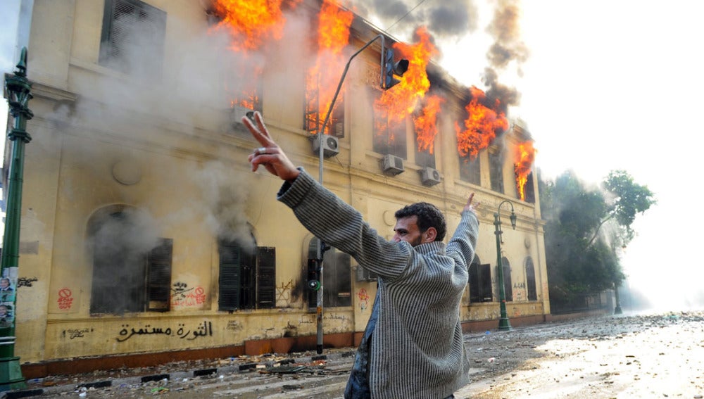 Un manifestante realiza el símbolo de la victoria frente a un edificio en llamas en El Cairo