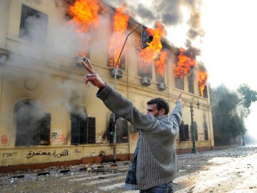 Un manifestante realiza el símbolo de la victoria frente a un edificio en llamas en El Cairo