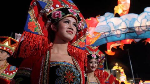 Una mujer con el traje tradicional da la bienvenida a las celebraciones de la v&iacute;spera
