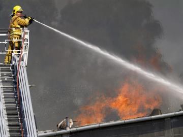 Un bombero echa agua sobre el incendio de la fábrica de puertas "Portas Vilanova"